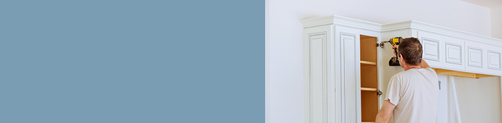 man using power drill on hinge of white cabinet door